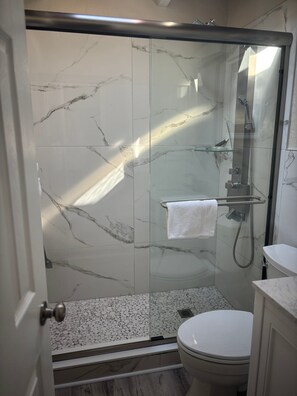 Ein modernes Badezimmer mit einer gläsernen Duschkabine, einer Toilette und einer Wand mit Marmorplatten.