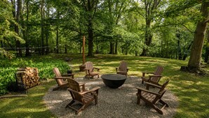 Zona circular amb seients d'estil Adirondack i una xemeneia, envoltada per un cercle de grava en un jardí forestal.