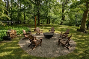 A circular seating area with Adirondack chairs and a fire pit, surrounded by a gravel circle in a forested garden.