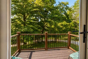 A wooden deck with a metal railing, overlooking a grassy area with trees.