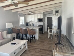 A modern kitchen with white cabinets, a microwave, stove, and a dining area with a white table and chairs. - SR-40, Lovely Courtside Unit (Siesta Key)