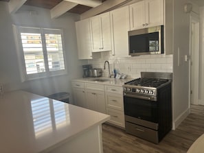 A kitchen with white cabinets, a stainless steel stove, a microwave, and a window with blinds. - SR-40, Lovely Courtside Unit (Siesta Key)