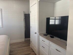 A bedroom with a bed, a TV on a dresser, and a door leading to a bathroom. - SR-40, Lovely Courtside Unit (Siesta Key)