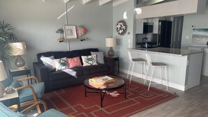 A modern living room with a sofa, chairs, a coffee table, and a kitchen area with a bar. - SR-41 Siesta Key 1BR condo with king bed, sleeper sofa, and courtyard views. (Siesta Key)