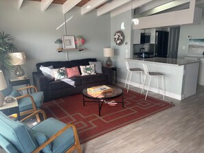 A modern living room with a sofa, chairs, a coffee table, and a kitchen area with a bar. - SR-41 Siesta Key 1BR condo with king bed, sleeper sofa, and courtyard views. (Siesta Key)