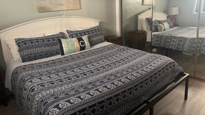 A bedroom with a bed, a bedside table, a mirror, and a painting on the wall. - SR-41 Siesta Key 1BR condo with king bed, sleeper sofa, and courtyard views. (Siesta Key)