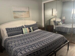 A bedroom with a bed, a bedside table, a mirror, and a painting on the wall. - SR-41 Siesta Key 1BR condo with king bed, sleeper sofa, and courtyard views. (Siesta Key)