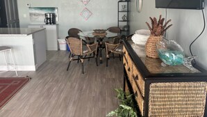 A modern kitchen with a dining area, featuring a round table, wicker chairs, and a bar area with a decorative glass pitcher. - SR-41 Siesta Key 1BR condo with king bed, sleeper sofa, and courtyard views. (Siesta Key)