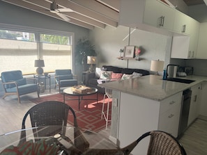 A modern kitchen with white cabinets, a central island, and a dining area with wicker chairs. - SR-41 Siesta Key 1BR condo with king bed, sleeper sofa, and courtyard views. (Siesta Key)