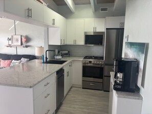 A modern kitchen with white cabinets, a stainless steel stove, a microwave, and a refrigerator. - SR-41 Siesta Key 1BR condo with king bed, sleeper sofa, and courtyard views. (Siesta Key)