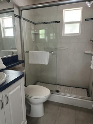 A bathroom with a glass-enclosed shower, a white toilet, and a vanity with a mirror. - SR-43 Stylish North Court Unit (Siesta Key)