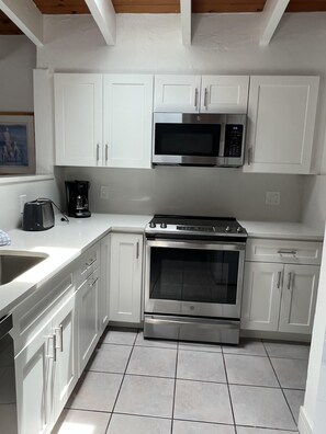 A modern kitchen with white cabinetry, a stainless steel oven, a microwave, and a coffee maker. - SR-43 Stylish North Court Unit (Siesta Key)