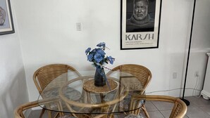 En matplats med ett runt bord i glas, omgivet av flätade stolar med blommiga kuddar.