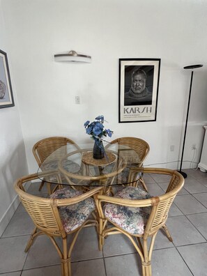 A dining area with a round glass table surrounded by wicker chairs with floral cushions. - SR-43 Stylish North Court Unit (Siesta Key)
