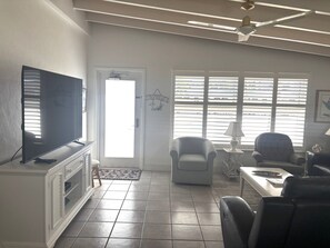 A living room with a television, two armchairs, a coffee table, and a door leading outside. - SR-43 Stylish North Court Unit (Siesta Key)
