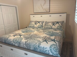 A bed with a floral and starfish pattern, a white headboard, and a door to the left. - SR- 44 1BR Siesta Key apartment with king bed and sleeper sofa. (Siesta Key)