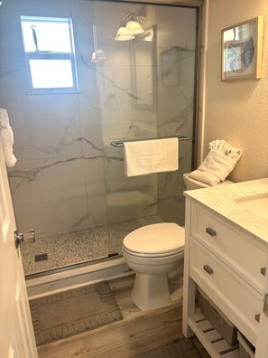 Ein Badezimmer mit einer gläsernen Duschkabine, einer Toilette, einem Waschbecken mit Marmorplatte und einem Handtuchhalter.