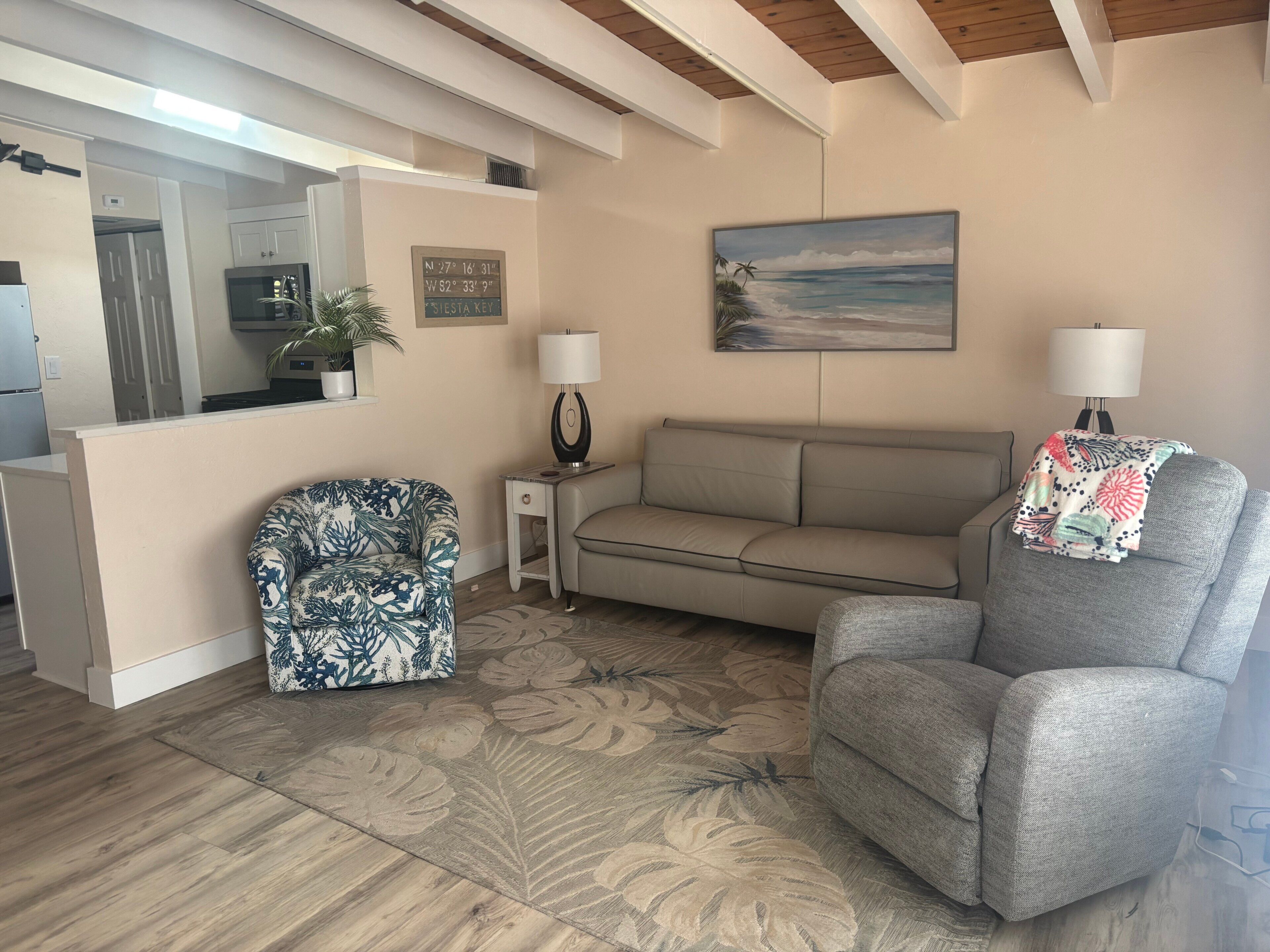Ein Wohnzimmer mit einer Couch, einem Sessel und einem Gemälde mit Strandmotiv.