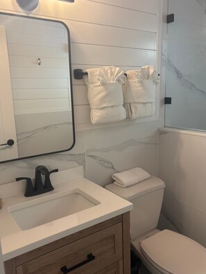 A bathroom with a white sink, a mirror, a toilet, and a towel rack with towels. - SR-45 - 1BR Siesta Key condo with king bed, sleep sofa, and courtyard views. (Siesta Key)