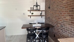 A dining area with a wooden table and four black chairs, a hanging light fixture, and a brick wall. - SR-45 - 1BR Siesta Key condo with king bed, sleep sofa, and courtyard views. (Siesta Key)