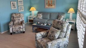 A living room with a blue wall, a sofa, a patterned armchair, a coffee table, and two side tables with lamps. - SR-46 -Cozy 1BR Siesta Key apartment with king bed and courtyard views. (Siesta Key)