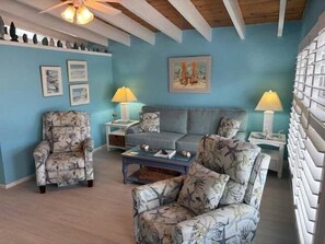 A living room with a blue wall, a sofa, a patterned armchair, a coffee table, and two side tables with lamps. - SR-46 -Cozy 1BR Siesta Key apartment with king bed and courtyard views. (Siesta Key)