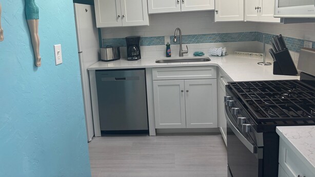 A kitchen with white cabinets, a built-in dishwasher, a stove, and a microwave. - SR-46 -Cozy 1BR Siesta Key apartment with king bed and courtyard views. (Siesta Key)