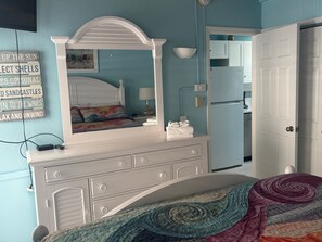 Une chambre à coucher comprenant un lit, une commode, un miroir et un mur orné d’un tableau et d’une affiche.