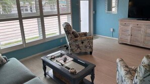 A living room with a sofa, armchair, and coffee table, a television, and a window with blinds. - SR-46 -Cozy 1BR Siesta Key apartment with king bed and courtyard views. (Siesta Key)