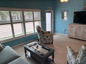 A living room with a sofa, armchair, and coffee table, a television, and a window with blinds. - SR-46 -Cozy 1BR Siesta Key apartment with king bed and courtyard views. (Siesta Key)