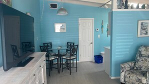 A room with a dining table and chairs, a white door, a blue wall, and a patterned armchair. - SR-46 -Cozy 1BR Siesta Key apartment with king bed and courtyard views. (Siesta Key)