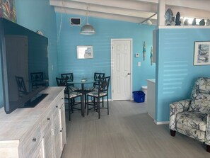 A room with a dining table and chairs, a white door, a blue wall, and a patterned armchair. - SR-46 -Cozy 1BR Siesta Key apartment with king bed and courtyard views. (Siesta Key)