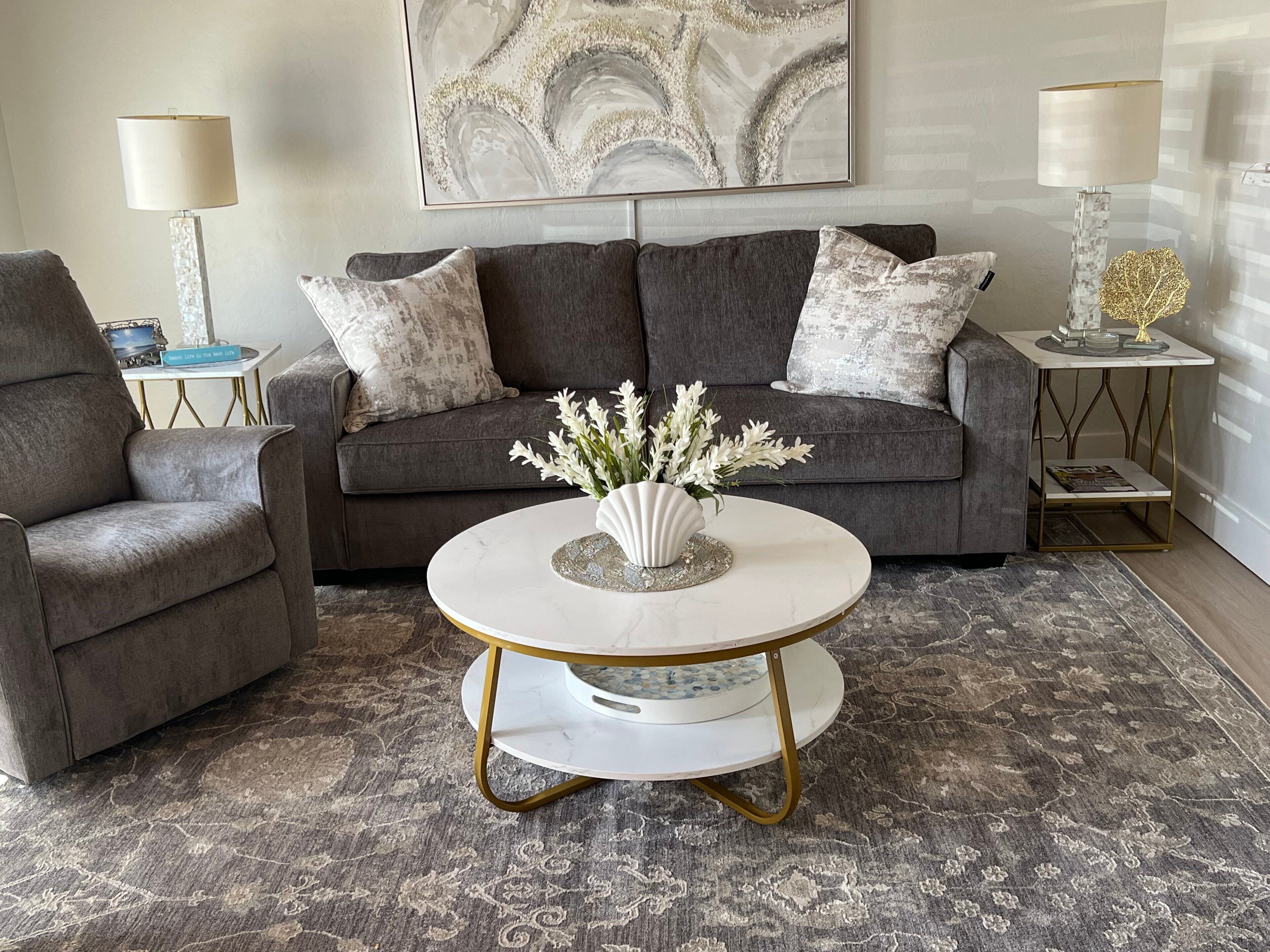 Un salón con un sofá gris, dos sillones, una mesa de centro redonda con un jarrón blanco y una alfombra estampada.