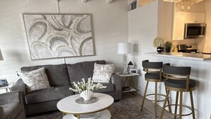Una sala de estar moderna con un sofá gris, una mesa de centro redonda y dos taburetes de bar.