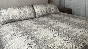 Un dormitorio con cama, mesita de noche, lámpara, puerta y un cuadro en la pared.