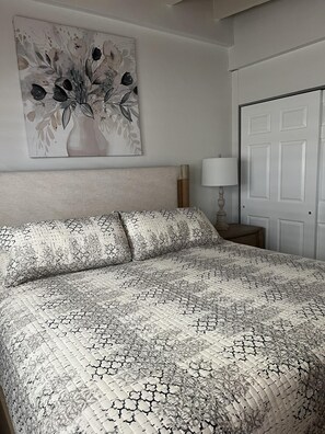 Ein Schlafzimmer mit Bett, Nachttisch, Lampe, einer Tür und einem Wandbild.