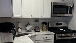 Una cocina con armarios blancos, microondas, estufa, licuadora y tostadora.
