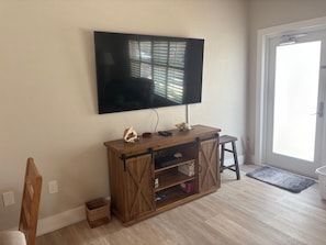 A living room with a mounted TV, wooden entertainment unit, and a door leading outside. - SR59 -1BR Siesta Key condo with courtyard view, queen bed, and sleeper sofa. (Siesta Key)