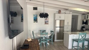 A modern kitchen with white cabinets, a stainless steel refrigerator, and teal chairs. - SR-50 -1BR 1BA Courtyard Unit (Siesta Key)