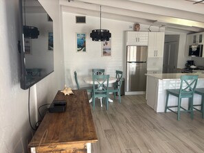 A modern kitchen with white cabinets, a stainless steel refrigerator, and teal chairs. - SR-50 -1BR 1BA Courtyard Unit (Siesta Key)