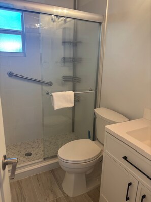A bathroom with a glass-enclosed shower, a toilet, and a sink. - SR-50 -1BR 1BA Courtyard Unit (Siesta Key)