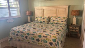 A bedroom with a bed, two nightstands, a window with blinds, and a wall sign. - 1BR Siesta Key condo with king bed, Murphy bed, courtyard views. (Siesta Key)