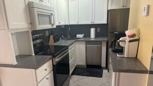 A compact kitchen with white cabinets, a microwave, a dishwasher, and a coffee machine. - 1BR Siesta Key condo with king bed, Murphy bed, courtyard views. (Siesta Key)