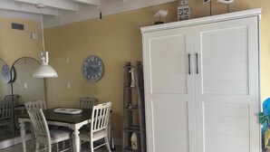 A dining area with a table, chairs, a clock, and a wardrobe. - 1BR Siesta Key condo with king bed, Murphy bed, courtyard views. (Siesta Key)
