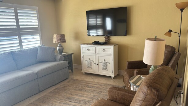 A living room with a sofa, armchair, TV, and a cabinet with decorative items. - 1BR Siesta Key condo with king bed, Murphy bed, courtyard views. (Siesta Key)