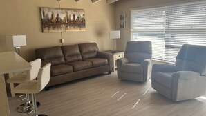 Ein Wohnzimmer mit braunem Sofa, zwei Sesseln, einem Couchtisch und einem Gemälde an der Wand.