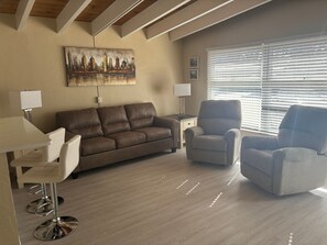 A living room with a brown sofa, two armchairs, a coffee table, and a painting on the wall. - 1BR Siesta Key condo with king bed, sleep sofa, and courtyard views. (Siesta Key)