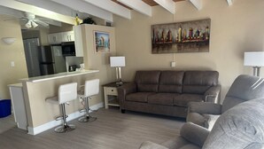 Ein modernes Wohnzimmer mit einer Couch, zwei Sesseln, einem Essbereich mit Bar und einem Stadtbild an der Wand.