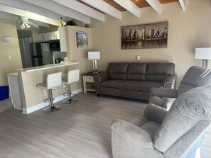 A modern living room with a sofa, two armchairs, a dining area with a bar, and a cityscape painting on the wall. - 1BR Siesta Key condo with king bed, sleep sofa, and courtyard views. (Siesta Key)
