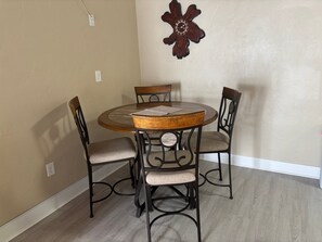 A dining area with a round table and four chairs, a wall clock, and a power outlet. - 1BR Siesta Key condo with king bed, sleep sofa, and courtyard views. (Siesta Key)